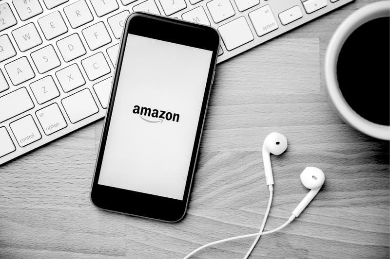 phone resting on keyboard with earphones and Amazon displayed on screen