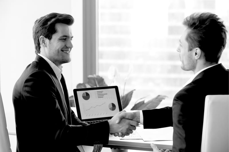 two smiling businessmen in suits shaking hands after sales meeting