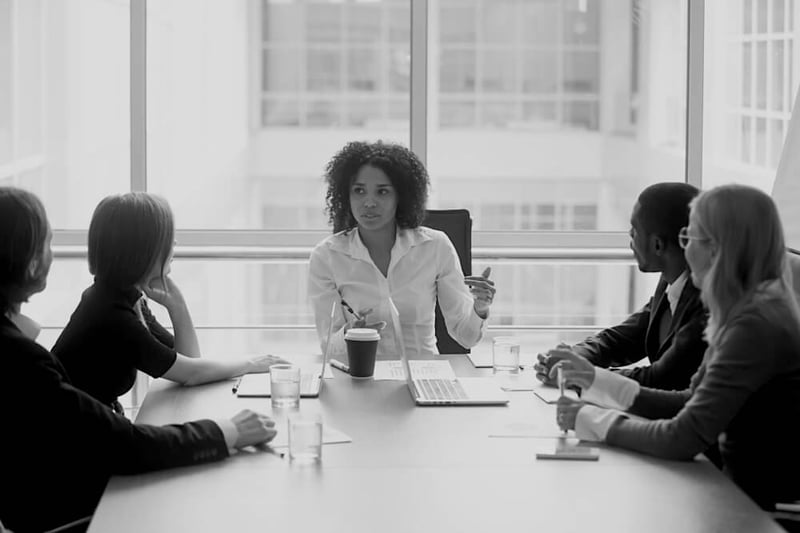 African American business woman leading team meeting at desk in front of a large window