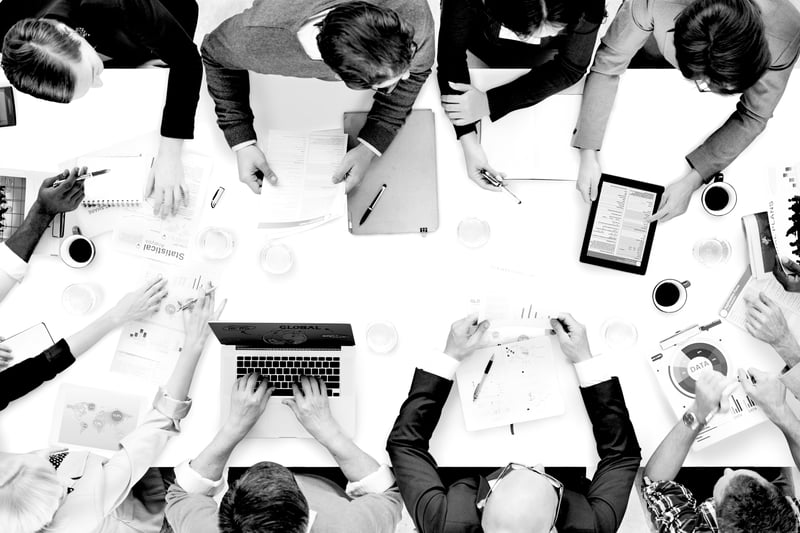 overhead view of group of workers at a desk brainstorming ideas with laptops and notepads