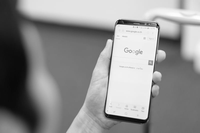 hand holding a cell phone with Google search engine displayed on screen
