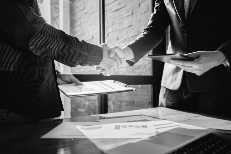 two marketing businessmen shaking hands in front of window