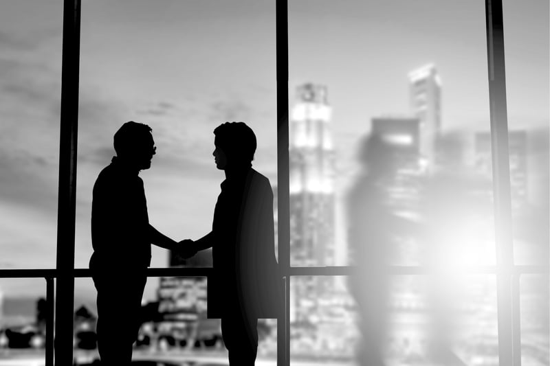 silhouette of two marketers shaking hands in front of office building window