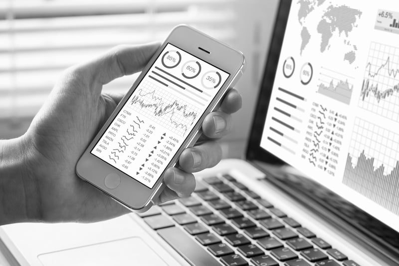 hand holding phone and computer screen displaying website metrics report