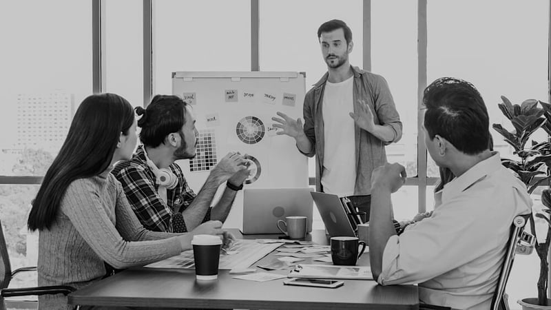 group of marketers at a table discussing branding strategy with laptops and whiteboard