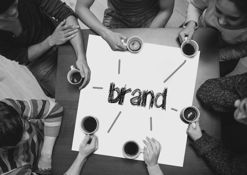 group of coworkers at desk with coffee cups and large paper that says brand