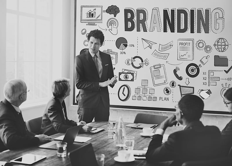 business man giving branding presentation on a white board to team of marketers sitting at a desk