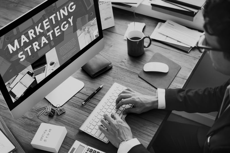 business man in suit typing at desktop computer with marketing strategy on screen