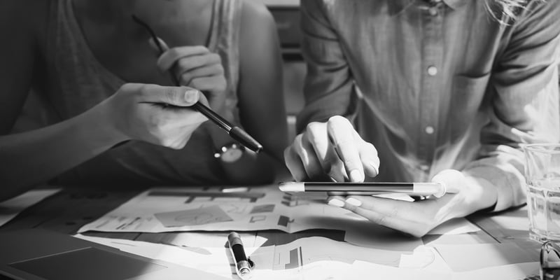 one marketer holding pen and another holding tablet at desk