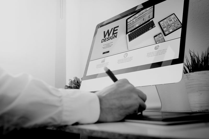 hand with pen writing on tablet in front of computer screen that displays web design