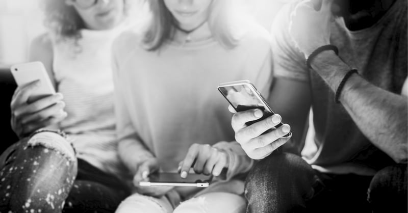 three people sitting together and looking at their cell phones