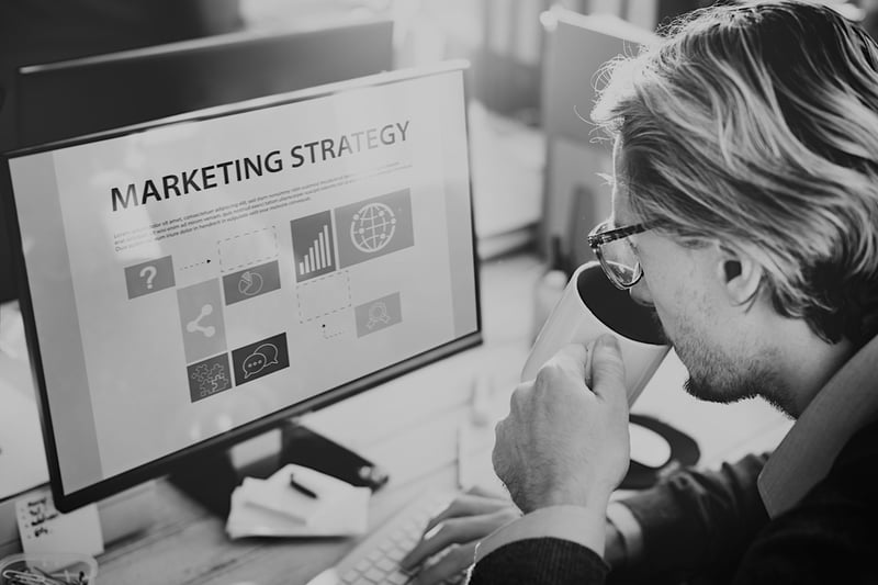 man sitting at desk drinking coffee and looking at computer screen with marketing strategy displayed 