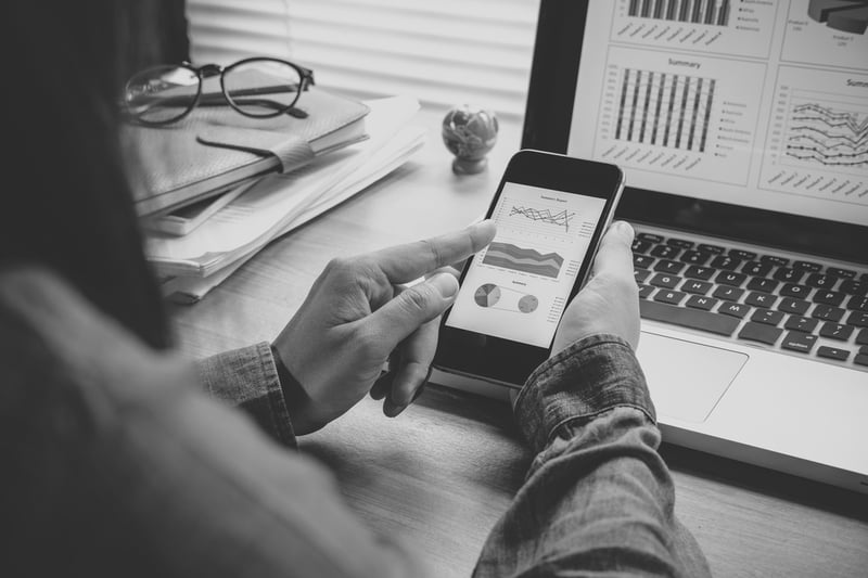 woman using cell phone and laptop to view website metrics performance at desk