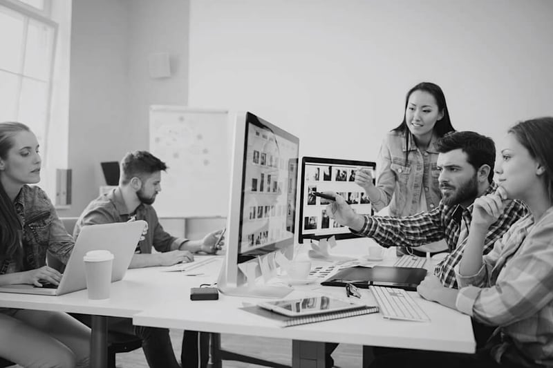 design and marketing team meeting at table with desktop computer and reviewing new designs