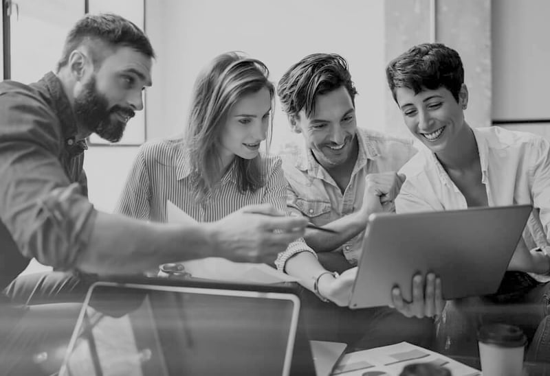 group of four excited and smiling marketers looking at a laptop screen together at an office desk