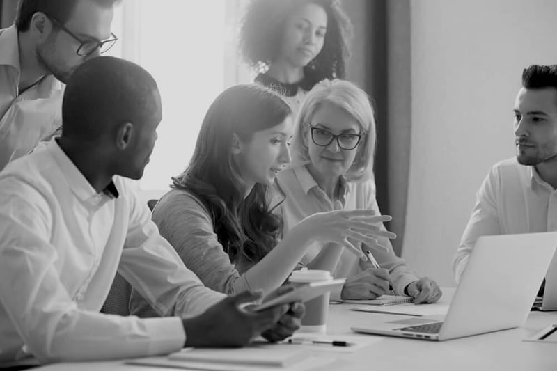 diverse group of female and male marketers meeting in front of laptop and discussing strategy