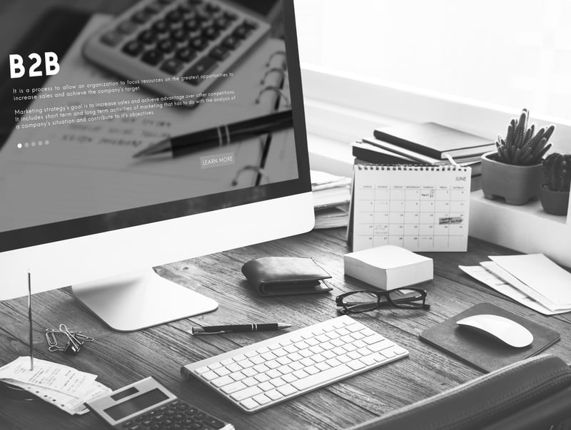 computer screen on desk with keyboard, pen, glasses, and calendar displays b2b marketing page