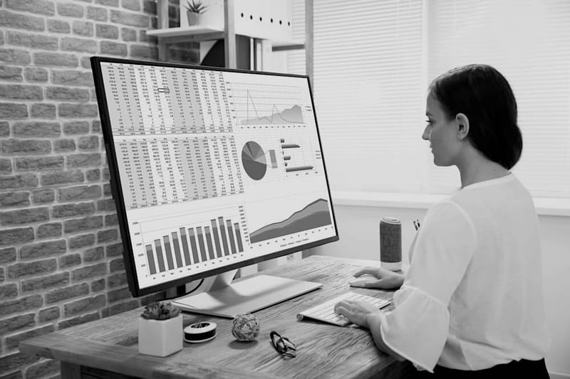 businesswoman at wooden desk on large desktop computer with marketing metrics on screen