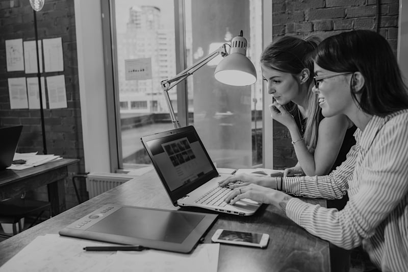 two female marketers on laptop at desk working on web design