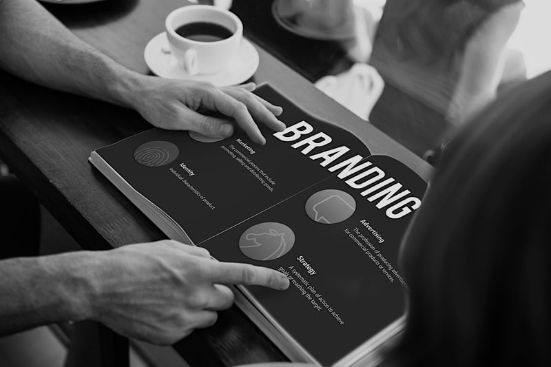 person pointing at branding book on desk with coffee cup