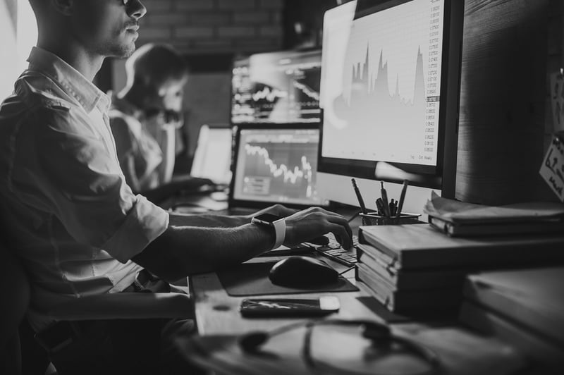 marketing man with glasses at desk in front of computer with analytics displayed on screen