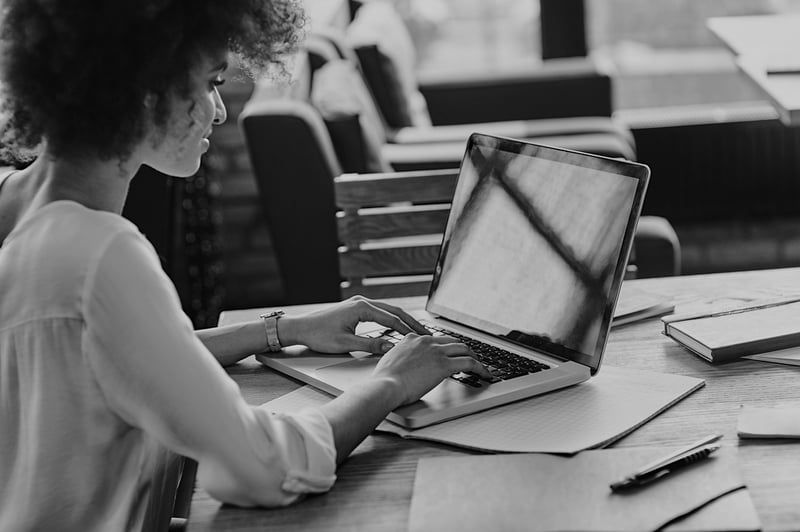 young woman with curly hair typing on laptop at a cafe desk alone