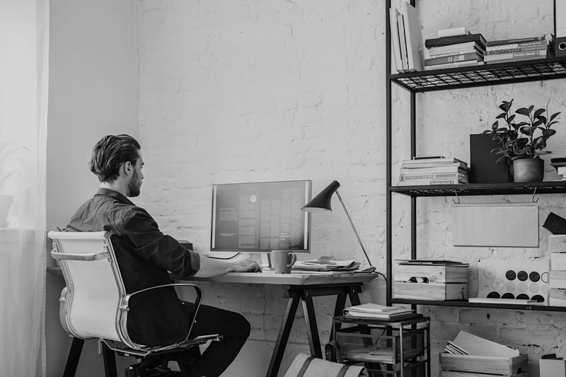 man working from home at desk computer in an office with many shelves and boxes